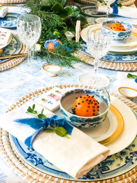 blue and white christmas table setting with white napkin and velvet ribbon and orange pomander