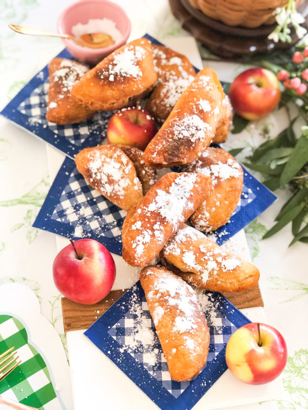 fried apple pies with powdered sugar placed on blue and white gingham napkins with whole apples