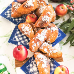 fried apple pies with powdered sugar placed on blue and white gingham napkins with whole apples