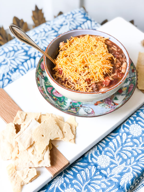 chili in a bowl with cheese on top served with crackers on a blue tablecloth and white board