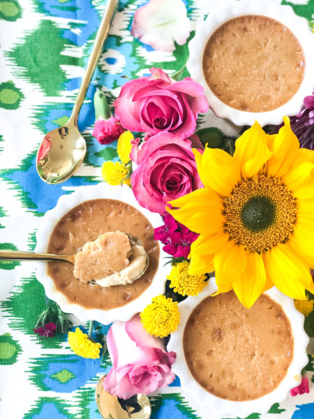 3 ramekins of caramel pots de creme surrounded by flowers and spoons