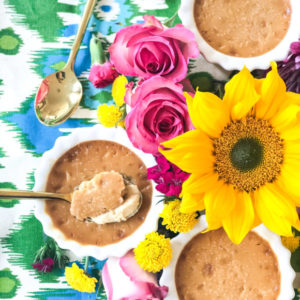 3 ramekins of caramel pots de creme surrounded by flowers and spoons