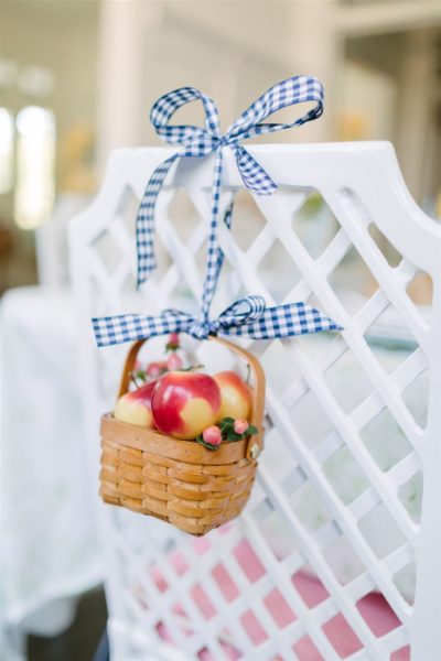 basket of apples tied to back of white chair with navy and white gingham ribbon