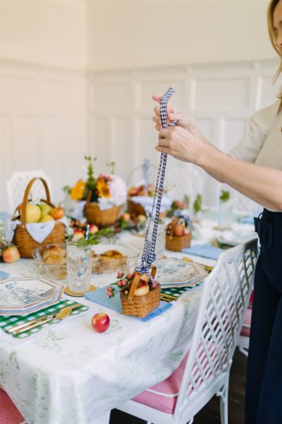 lady tying ribbon on handle of mini basket with mini apples inside at a party