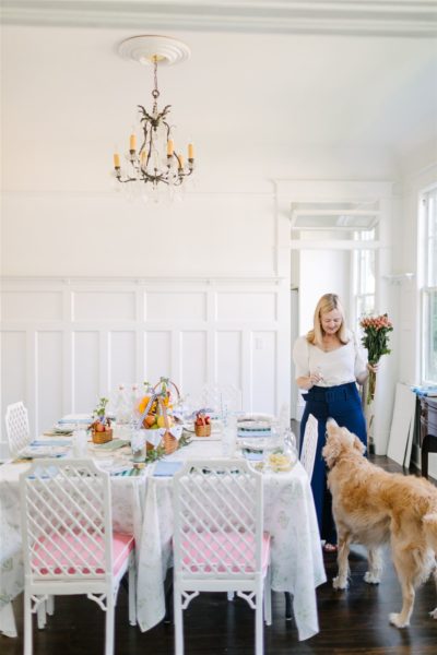 white dining room with table set lady holding flowers and golden retriever dog