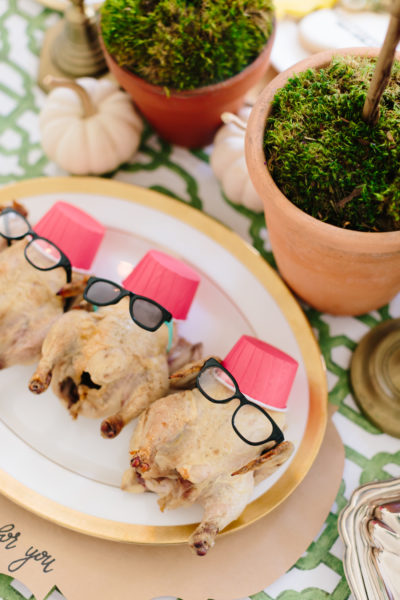 3 baked cornish hens with glasses and red hats on a white platter with gold rim