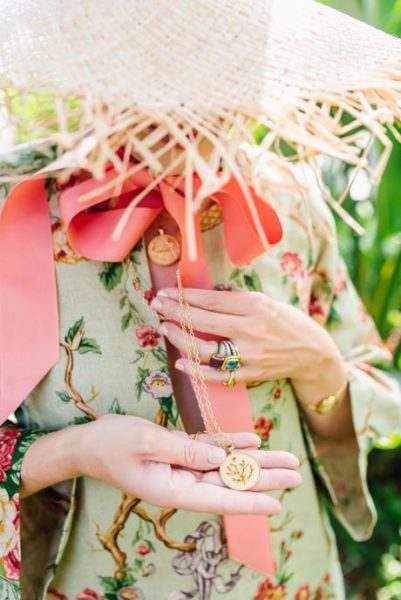 sarah bray wearing caftan and straw hat with coral ribbon showing gold necklace
