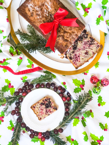 cranberry bread with a red bow around it and displayed on a christmas tablecloth with holly and cranberries
