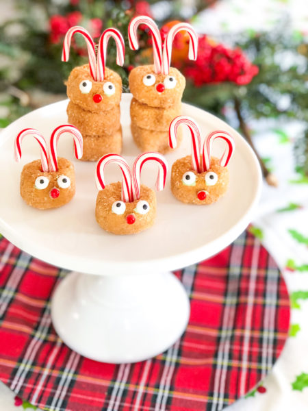 rudolph donuts with candy candes and candy eyes and nose on a white cake stand with plaid charger