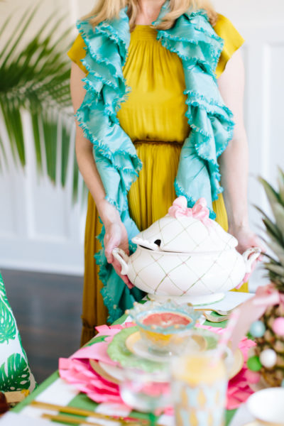 lady wearing yellow dress with turquoise scarf placing lidded serving dish on table