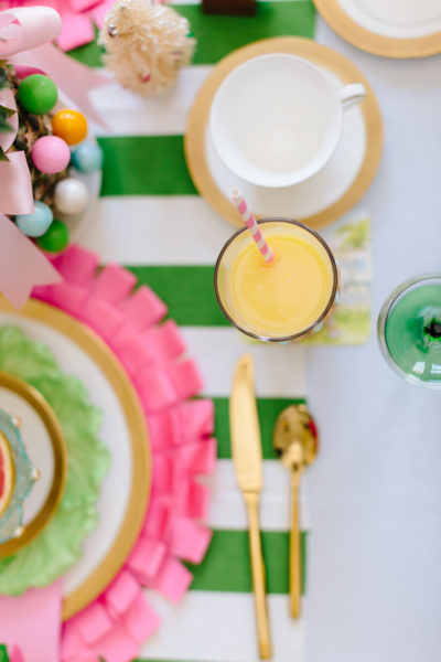 glass of orange juice with pink straw on table with pink and green