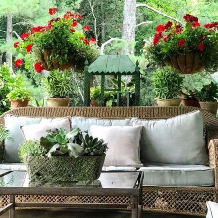 porch with hanging baskets of red geraniums and green plants