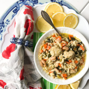 orzo soup with chicken meatballs and spinach on a plate with lemons and a napkin