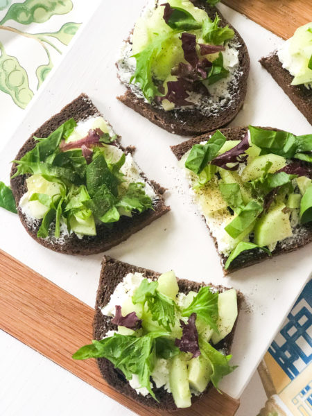 pumpernickel bread slices cut in half with cheese lettuce on white cutting board