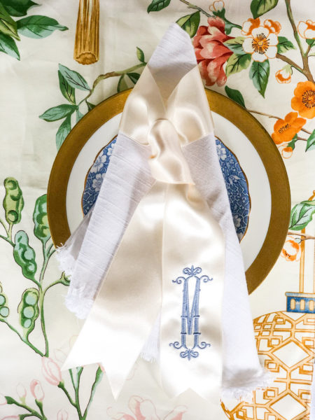 white napkin with monogrammed ribbon twilly on plates with floral tablecloth
