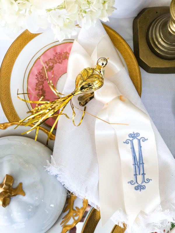 stack of plates with white napkin with ribbon and metallic bird ornament
