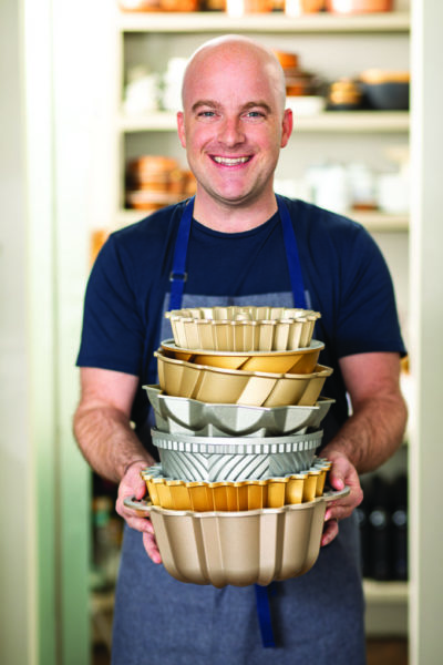brian hart hoffman standing in in his kitchen holding a stack of bundt pans