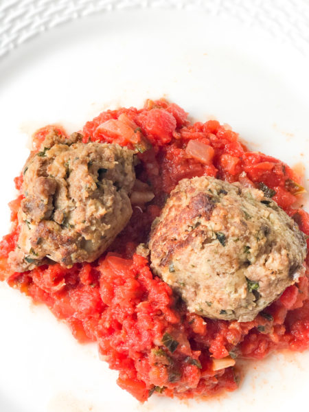 2 italian meatballs on top of marinara sauce on a white plate