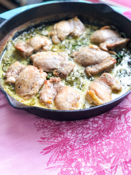 skillet of ckicken with spinach on bright pink kitchen towel