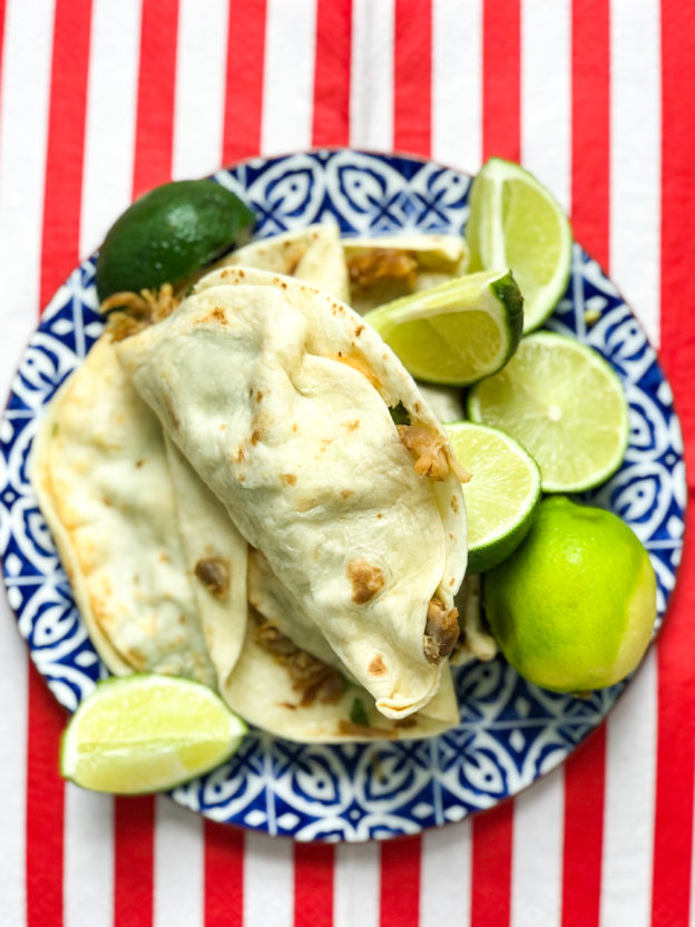 pork carnitas with limes on blue plate red white stripe background