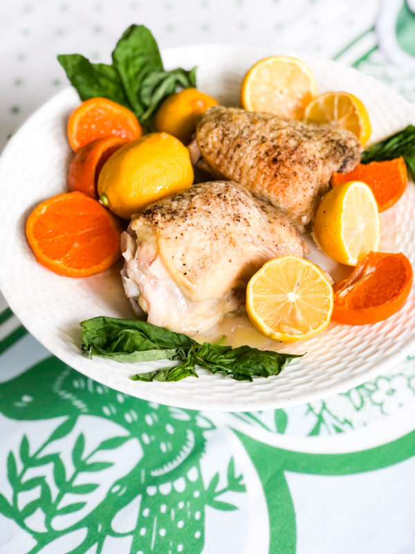 baked chicken on white plate with orange and lemon slices and basil