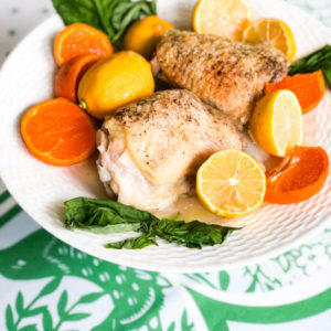 baked chicken on white plate with orange and lemon slices and basil