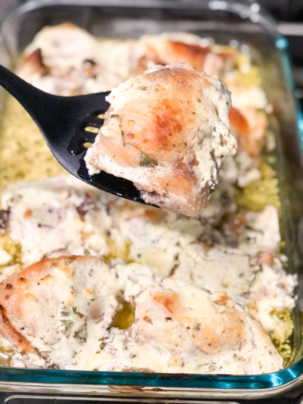 baked chicken thighs marinated with plain yogurt in casserole dish with one piece being held on a black spatula