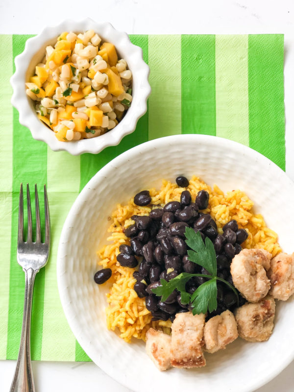 chicken with yellow rice and black beans with mango salsa on the side in a bowl