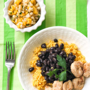 chicken with yellow rice and black beans with mango salsa on the side in a bowl