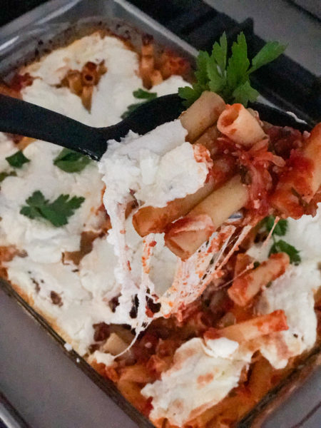 baked ziti being served from pan with melted cheese stretched