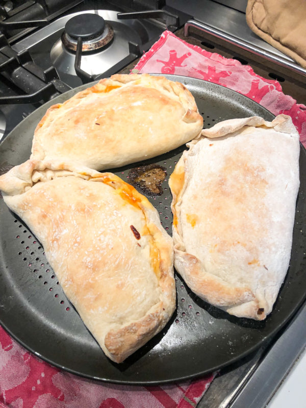 three calzones on a pizza pan on top of oven