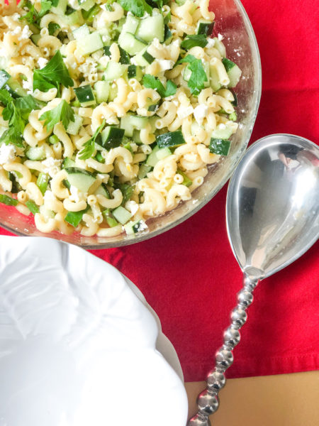 pasta salad in clear bowl with silver serving spoon on red tablecloth