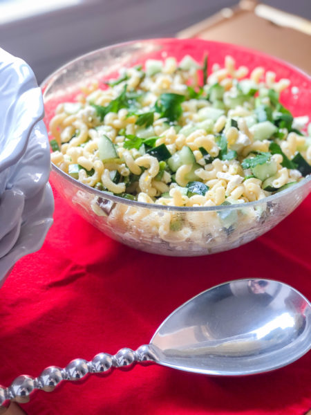 pasta salad in large clear bowl on red napkin with large silver serving spoon