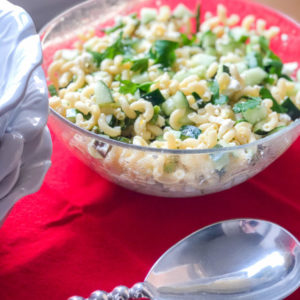 pasta salad in large clear bowl on red napkin with large silver serving spoon