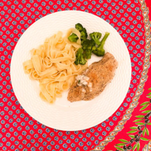 chicken with cream cheese broccoli and egg noodles on white plate and red floral tablecloth