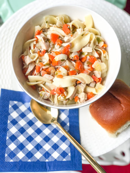 chicken noodle soup with blue and white gingham napkin spoon and bread