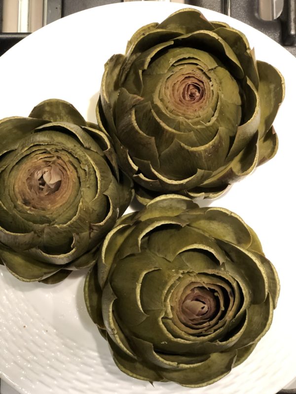 three artichokes served on a white plate