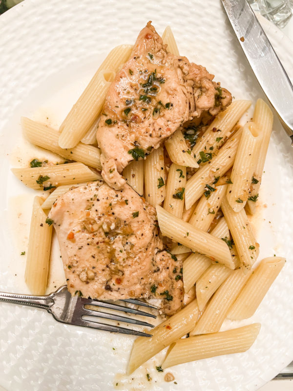 chicken with garlic butter and parsley over pasta on white plate with silver fork and knife