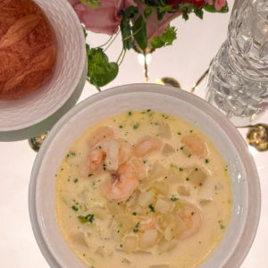 shrimp chowder on table in white bowl with bread on plate beside bowl