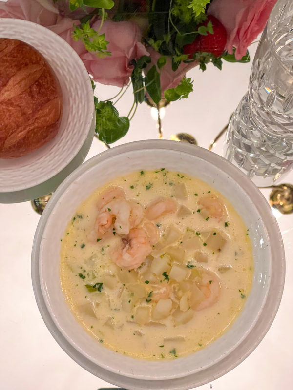 shrimp chowder on table in white bowl with bread on plate beside bowl