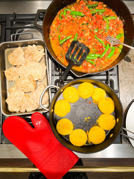 ingredients on stove for polenta chicken with tomato sauce and red oven mitt