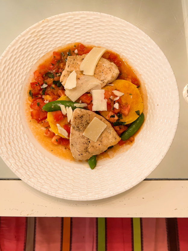 roasted chicken with polenta cakes and tomato sauce on white plate on table with mirrored top