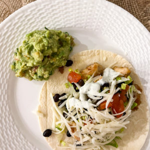 chicken soft tacos with black beans lettuce cheese tomato white sauce and a side of guacamole