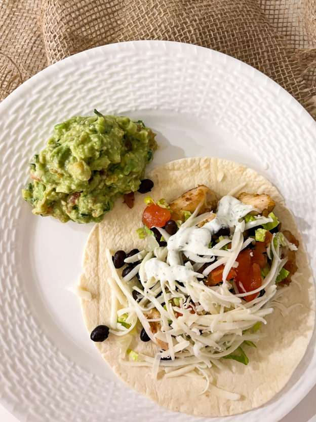 chicken soft tacos with black beans lettuce cheese tomato white sauce and a side of guacamole