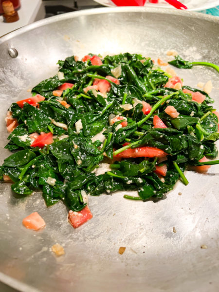 tuscan spinach cooked in a silver skillet with tomatoes and parmesan cheese