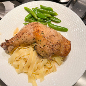 whole baked chicken leg with egg noodles and sugar snap peas on a white plate