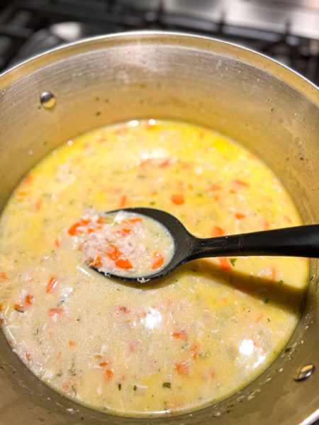 creamy chicken soup in sliver pot on stove with large black serving spoon in soup