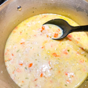 creamy chicken soup in a pot being stirred with large black spoon