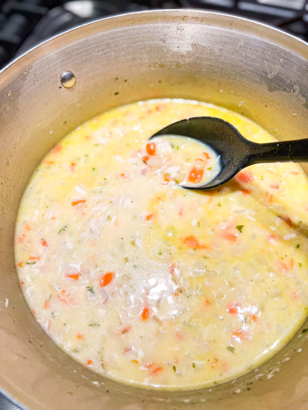 creamy chicken soup in a pot being stirred with large black spoon