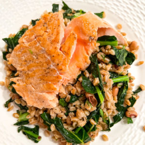 salmon served over a bed of farro with kale and black eyed peas